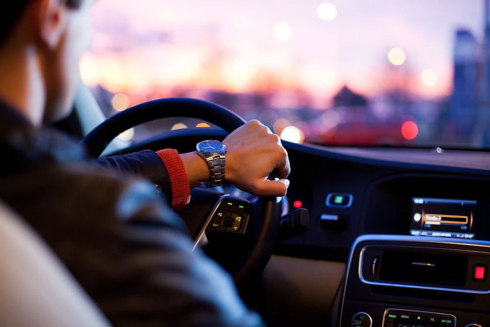 A driver's hand on the steering wheel at dusk